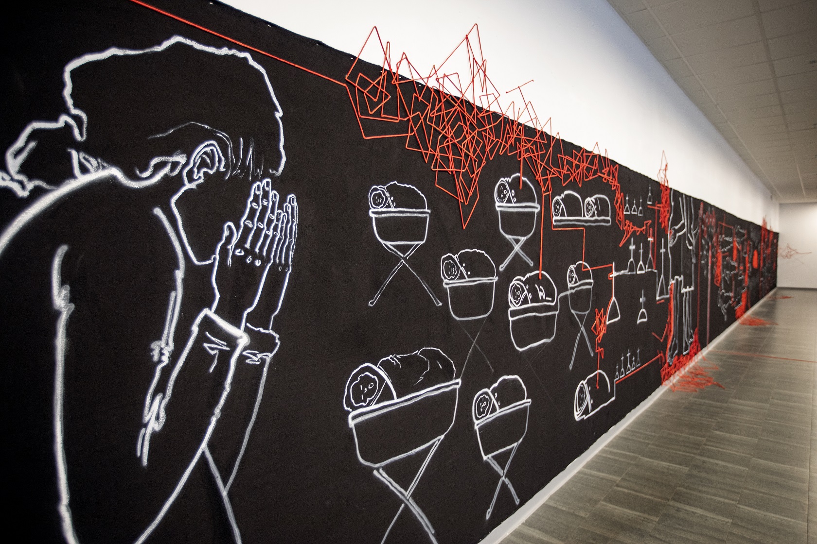 Black canvas stretching over 20 meters with white paintings and red lines. A grieving woman is seen closest in picture.