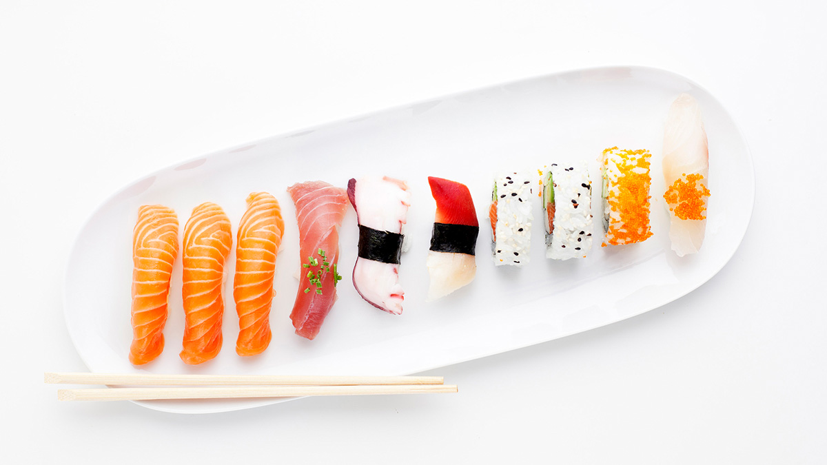 Avlång tallrik med olika sorters sushi med fisk, och ätpinnar. 