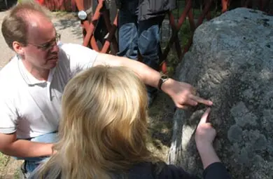 Två personer sitter på huk och pekar på en detalj på en stor sten. 