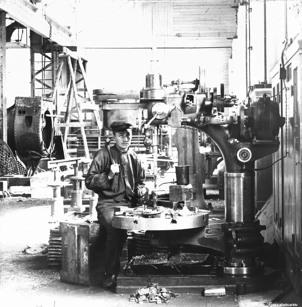 En arbetare sitter i en verkstad vid en stor borrmaskin.