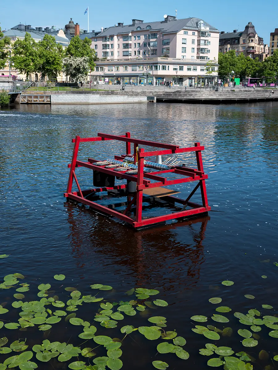 En kantig skulptur byggd av en röd ställning är placerad på vattenytan.