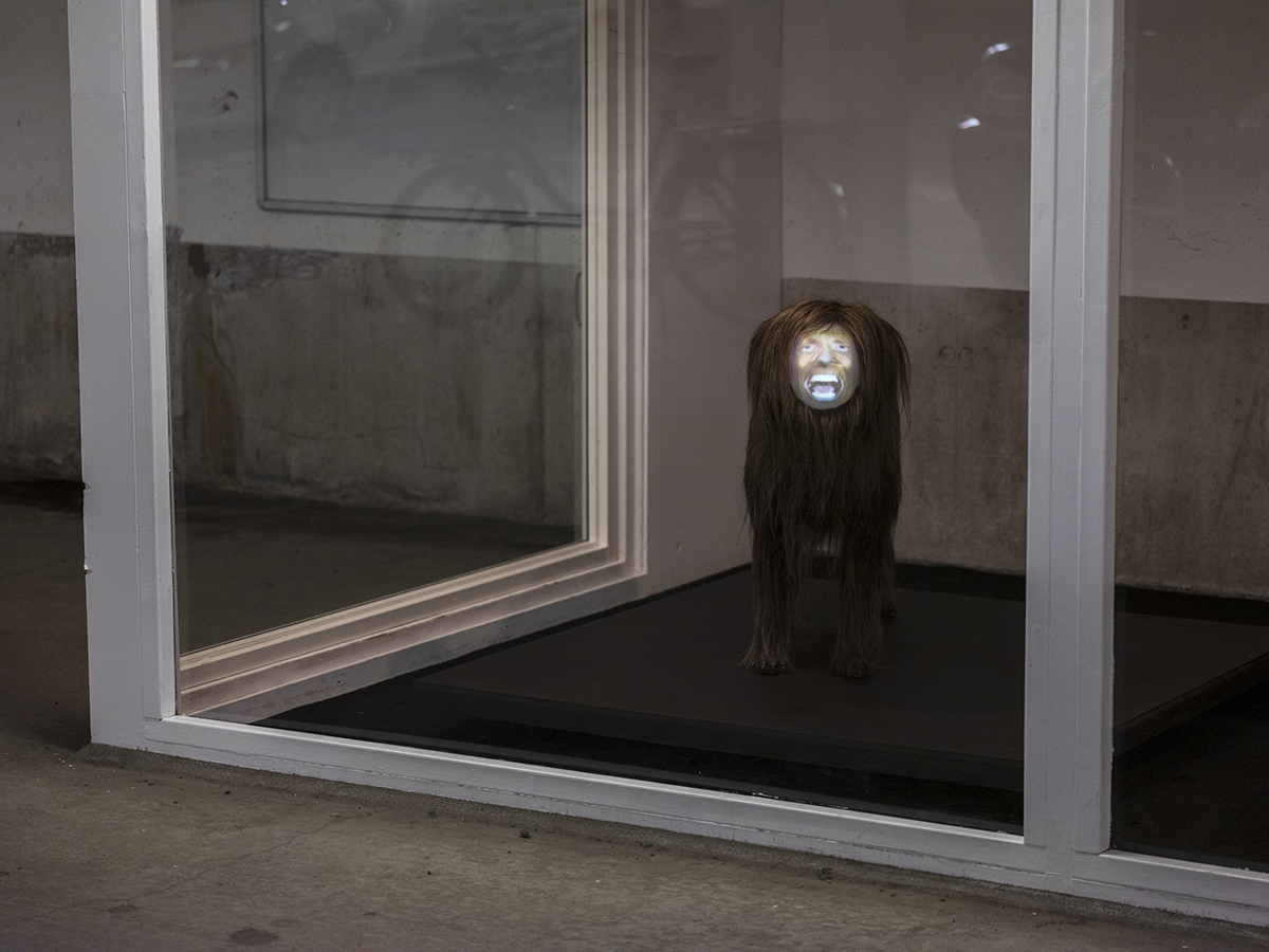 En djurliknande skulptur med ett lysande ansikte syns innanför ett inglasat rum