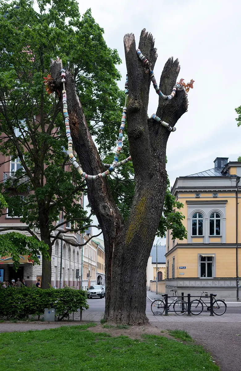 I ett träd med avkapade grenar hänger ett överdimensionerat pärlhalsband i olika färger