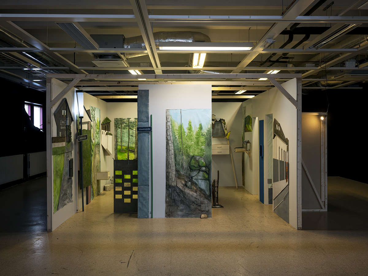 I ett stort rum står en installation bestående av några uppställda mindre väggar. På väggarna finns olika objekt uppsatta, däribland flera större tavlor, hyllor, husskulpturer och en lyktstolpe. Tavlorna föreställer olika skogsmotiv samt har stark ljusgrön färg.