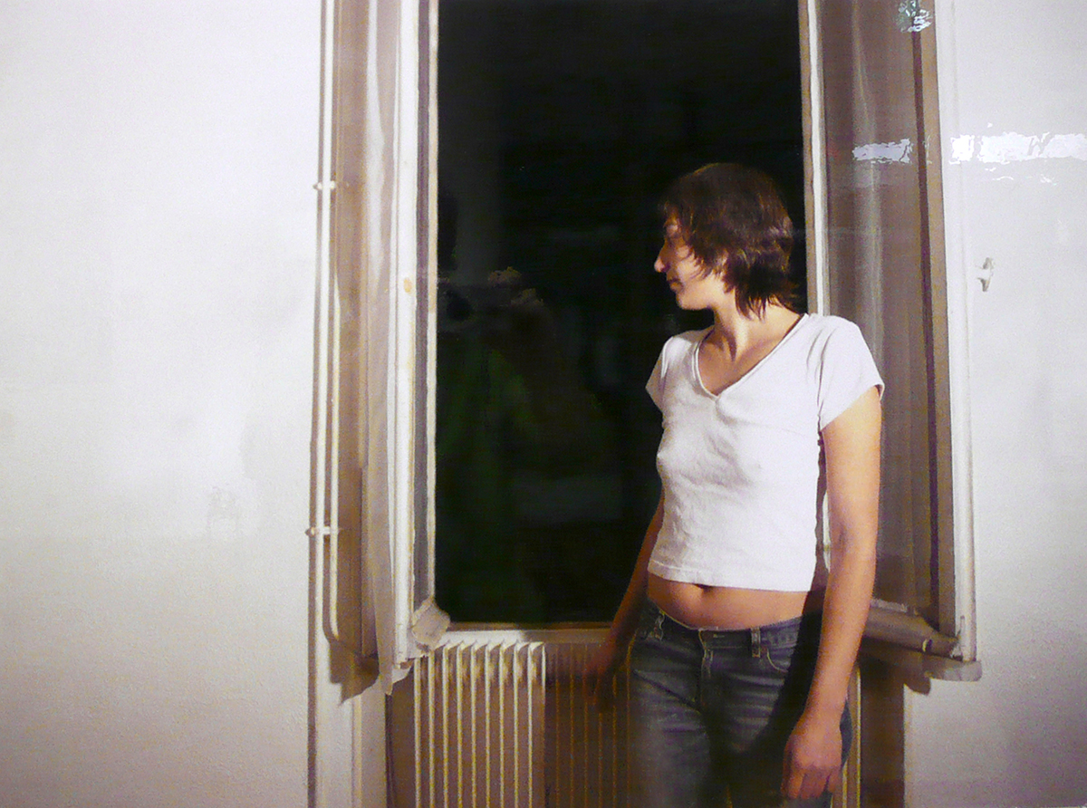 Ett fotografi av en kvinna som står vid ett fönster.