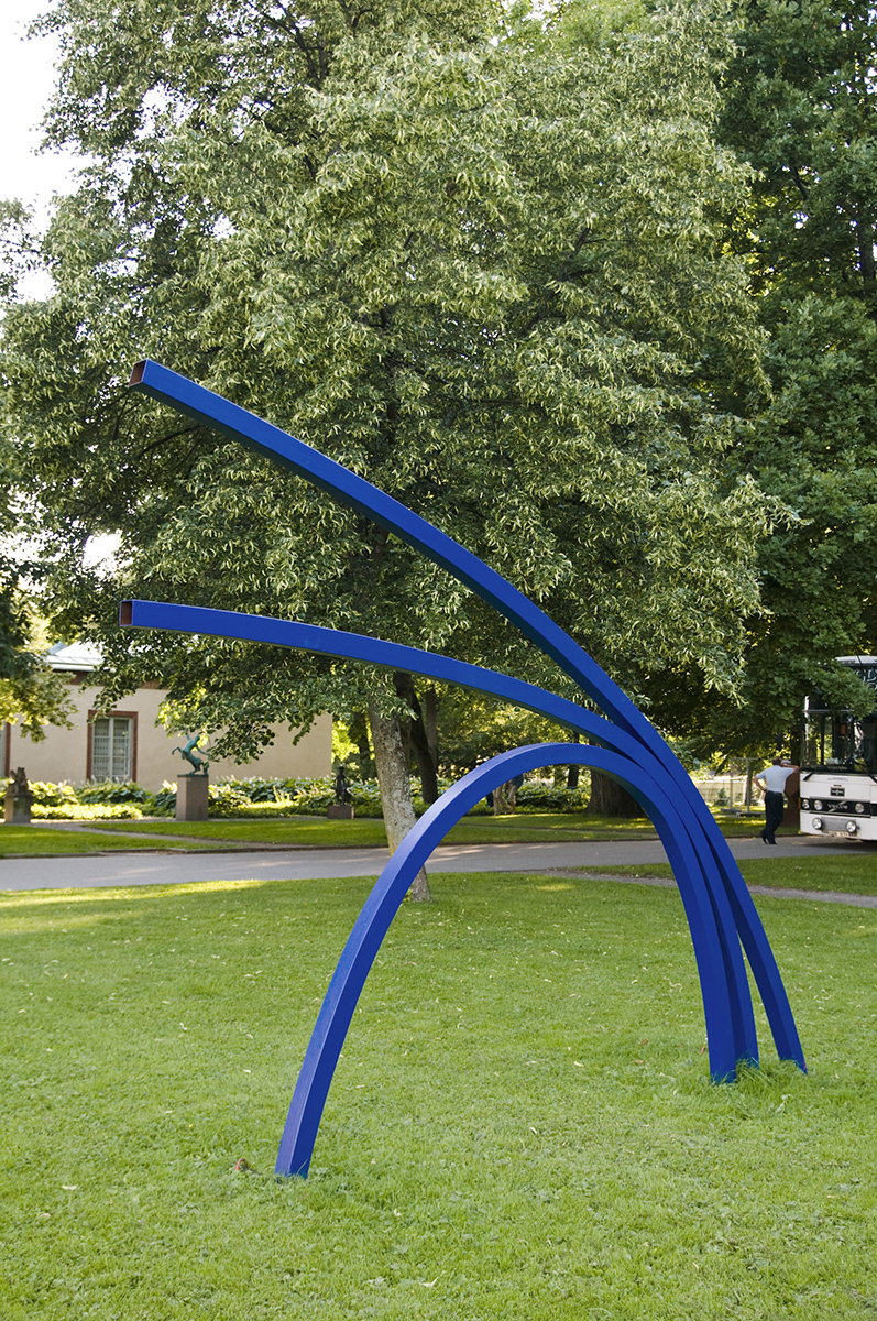På en gräsmatta står en staty av tre blåa fyrkantiga stångar.