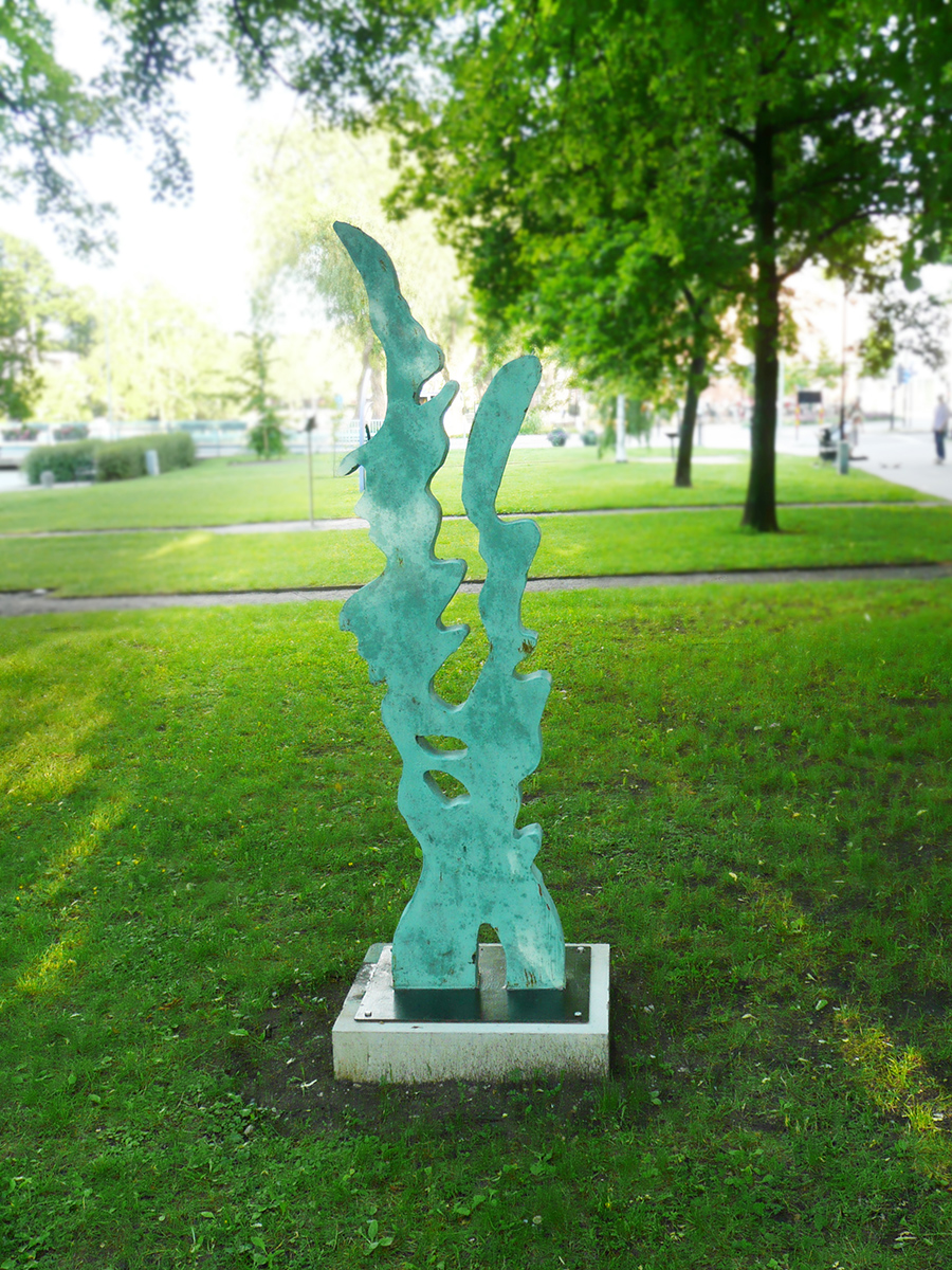 På en gräsmatta står en grön skulptur formad som två vågor fast att de går uppåt. 