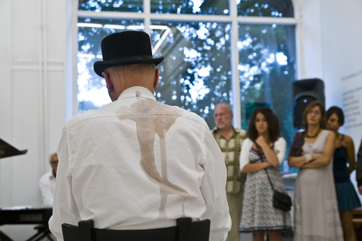 Fotot är taget så man ser baksidan av en man med svart hatt samt som har fått en stor fläck på sin skjorta.