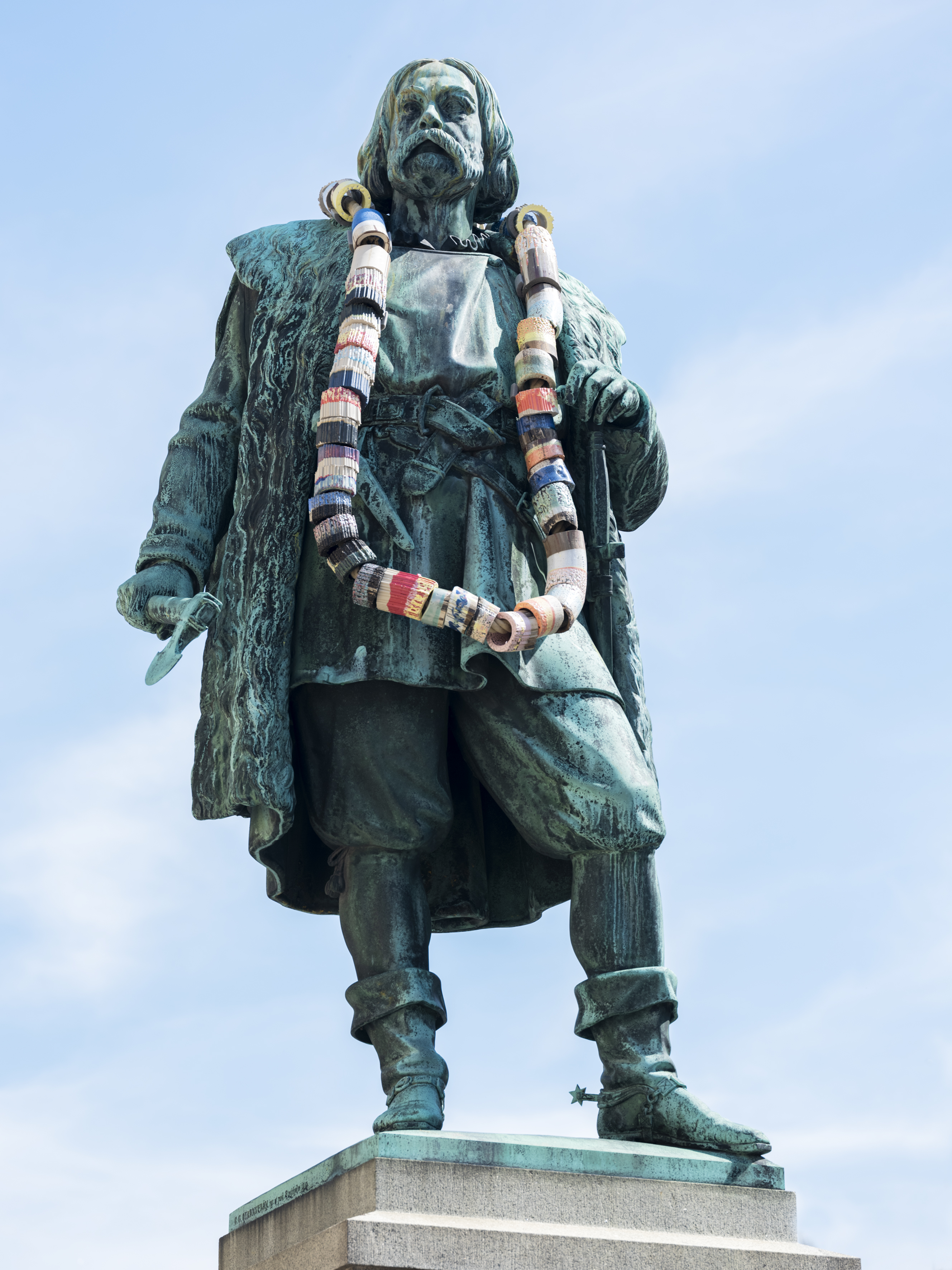 En bronsstaty föreställande Engelbrekt har på sig ett överdimensionerat halsband med stora pärlor i olika dova färger, bakom statyn är himlen blå