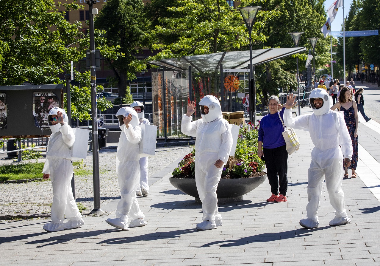 På Järntorget utförs ett grupp-performance där fem människor utklädda till astronauter går runt och hälsar på alla civila människor. 