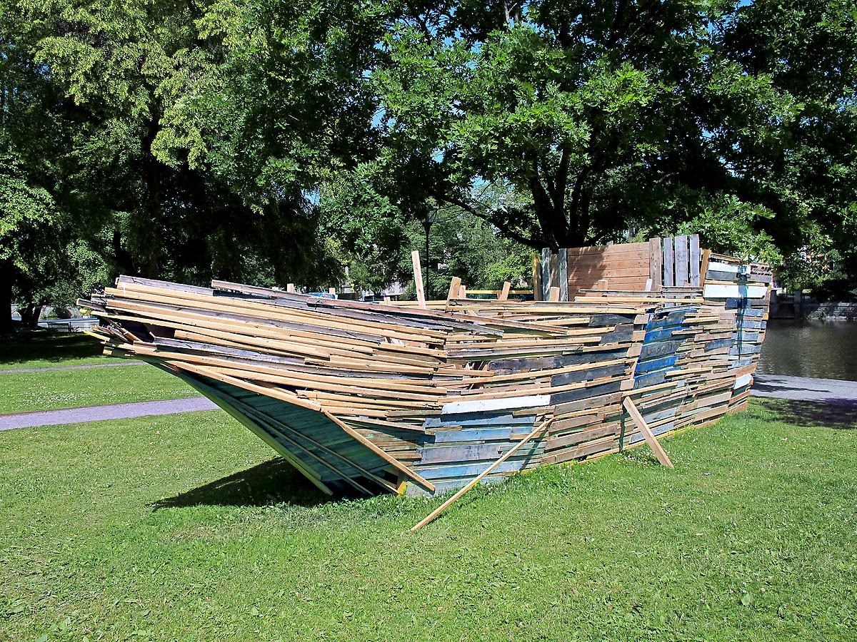Utomhus på en gräsmatta längs Svartån står ett stort konstverk av en ark. Båten är bygg av massa olika plankor i olika färger. 