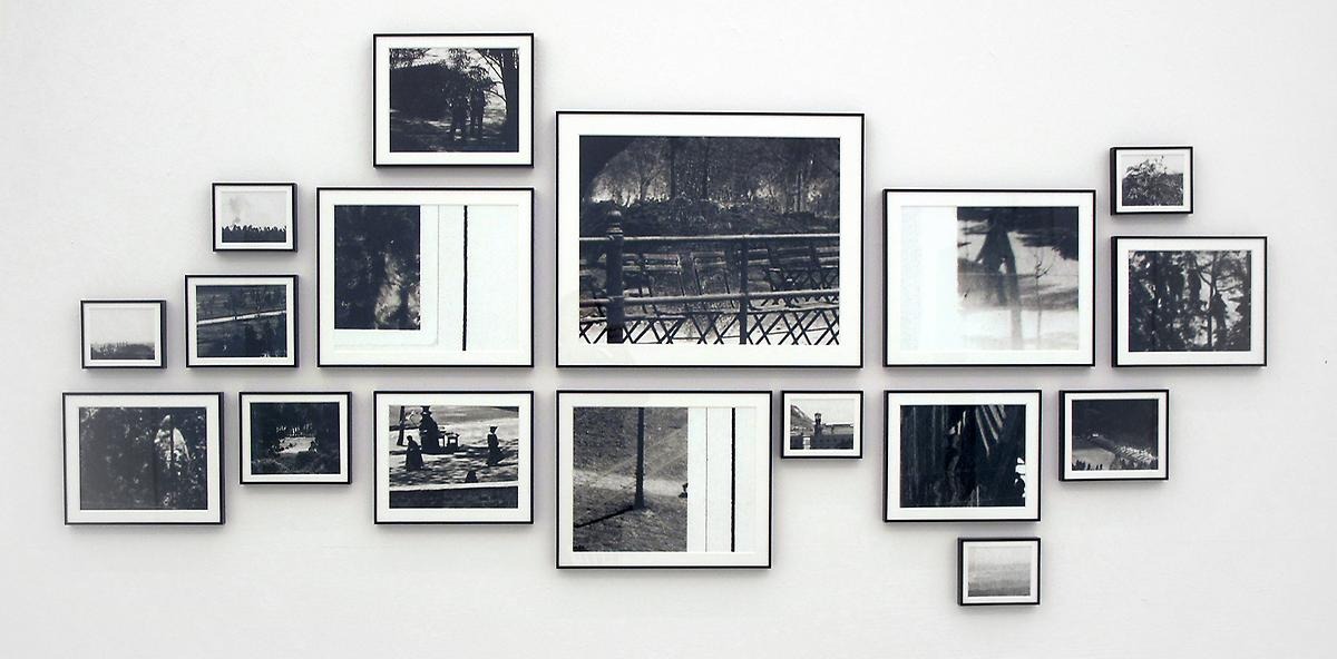 På en vitt vägg hänger 17 stycken svart vita fotografier i en varsin svartram. Fotografierna är i olika storlekar och föreställer olika miljöer utomhus.