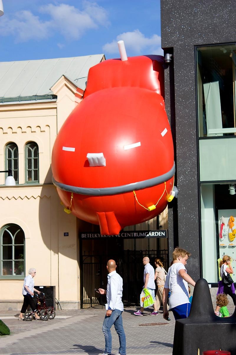 En stor uppblåst röd Zeppelinare trycker sig ut genom en gränd mellan två byggnader.