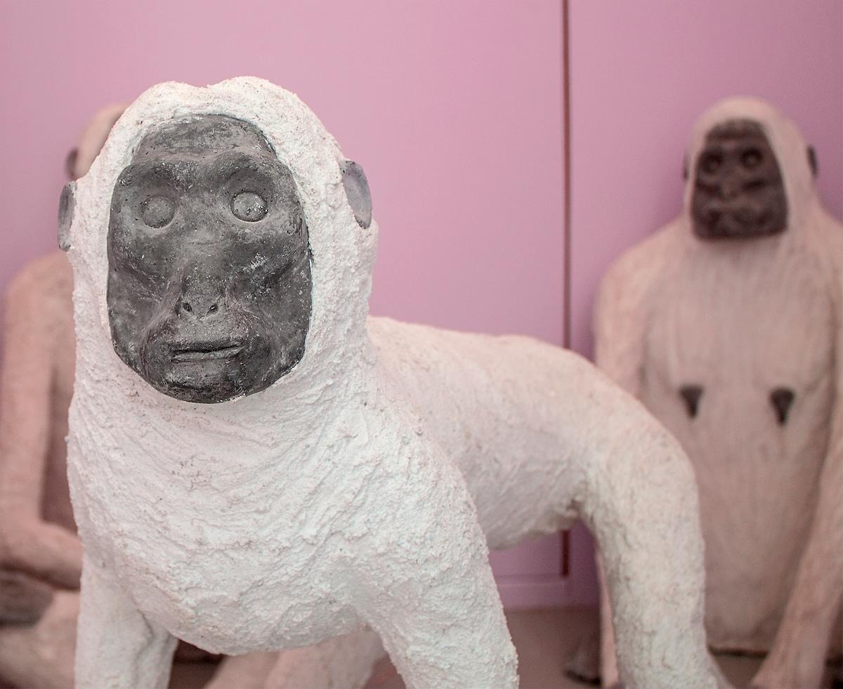 En närbild på en apa skulptur som står på alla fyra och har vitkropp och svart ansikte. I bakgrunden står två apor till. 