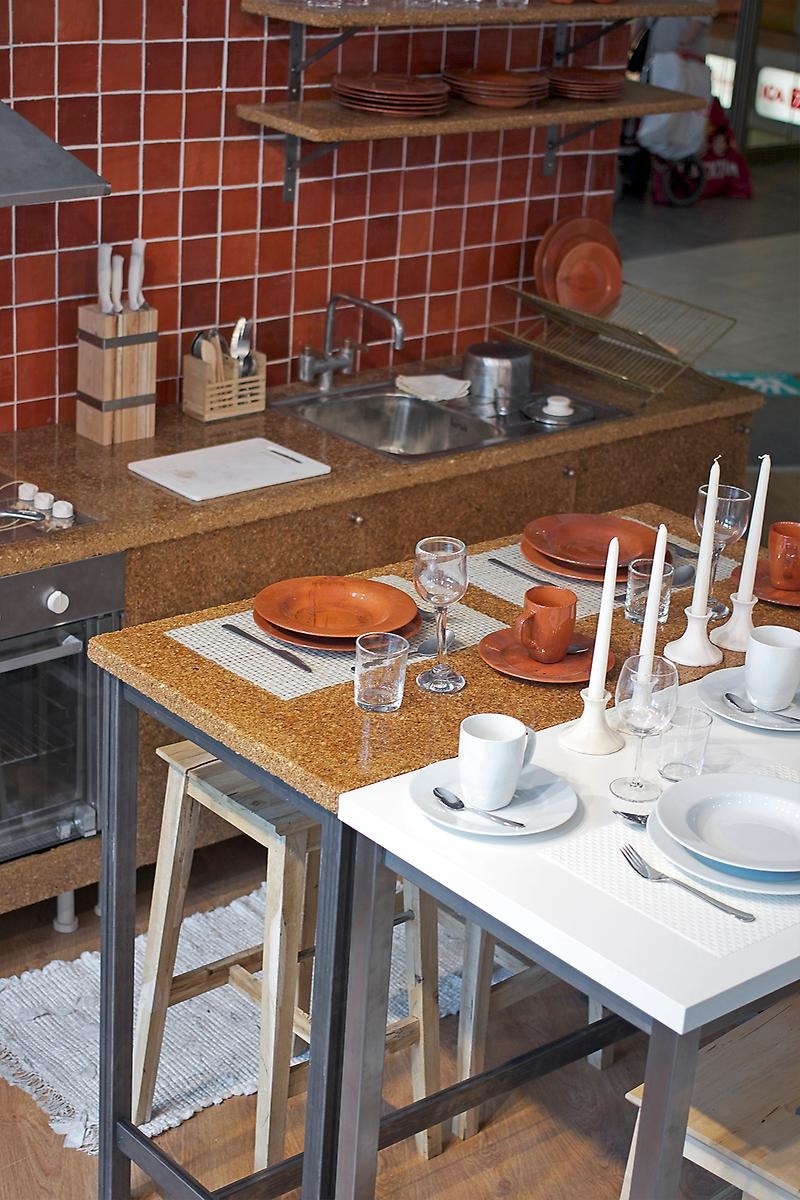 Konstnären Strandahls har skapat en handgjord kopia av ett IKEA-kök och färgerna går i brunt och orange. Köket innehåller allt ett kök behöver samt ett klar dukat avlångt matbord och mitt emot det står ett vitt nutida IKEA matbord med deras klassiska porslin.