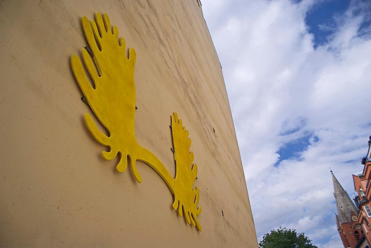Högt upp på en fasad sitter en gul skulptur som liknar en abstrakt krabba.