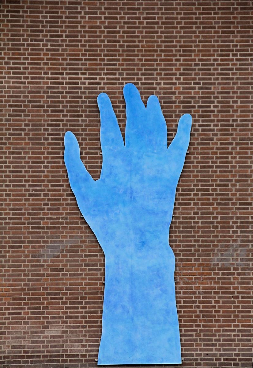På en tegelfasad hänger en skulptur av en blå hand.