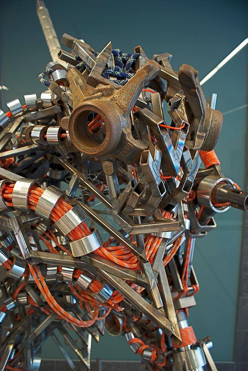 En robot liknande skulptur som är uppbyggd av ett rödvit rep som går igenom tjocka skinande aluminium ringar. 