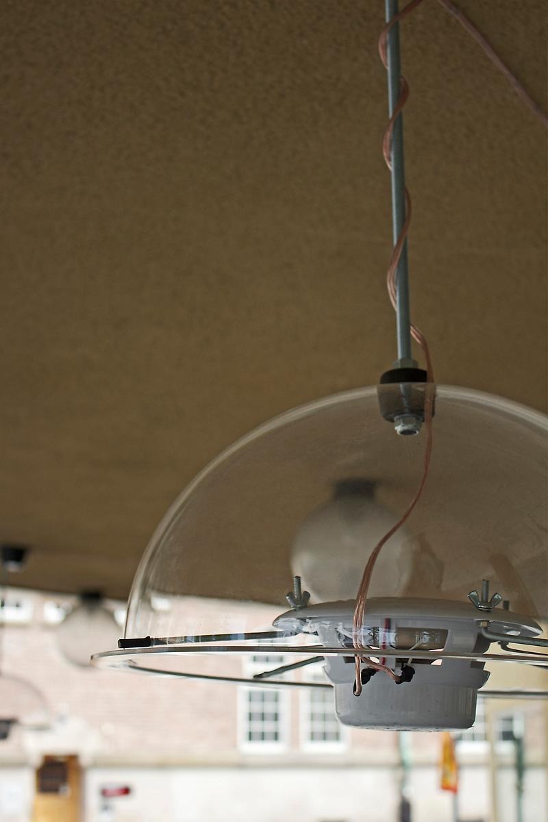 Från ett tak hänger en rund ställpinne ner och längst ner på pinnen sitter en genomskinlig glaskupa. I denna kupa sitter en ljudinstallation som spelar in ljud.