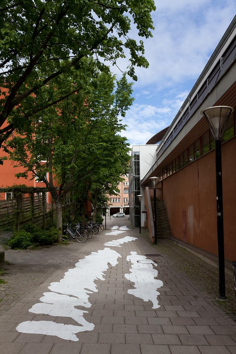 På en gånggata är vita skuggliknande siluetter målade på marken. 