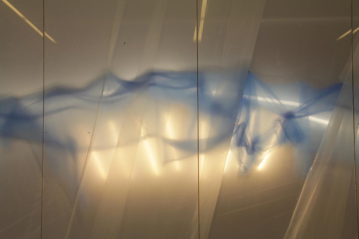 Ett fotografi på en reflektion av en blå våg bakom ett vitt tygstycke. 