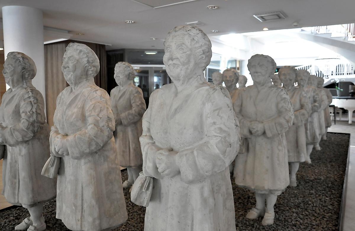 I ett rum står skulpturer av tanter på rad. Tanterna står i likadana ställningar med händerna ihop och all har en varsin handväska. 
