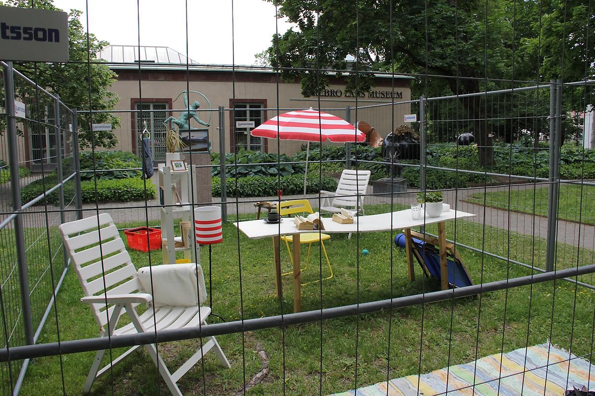 På en gräsmatta framför Örebro läns museum står ett grått stängsel placerat så det skapar en kvadrat. I kvadraten står många olika möbler som bygger upp olika scener. Tillexempel i ett hörn står en vit solstol tillsammans med ett vitrödrandigt parasoll. I mitten står ett vit skrivbord på det står en planta, en kopp och böcker. 