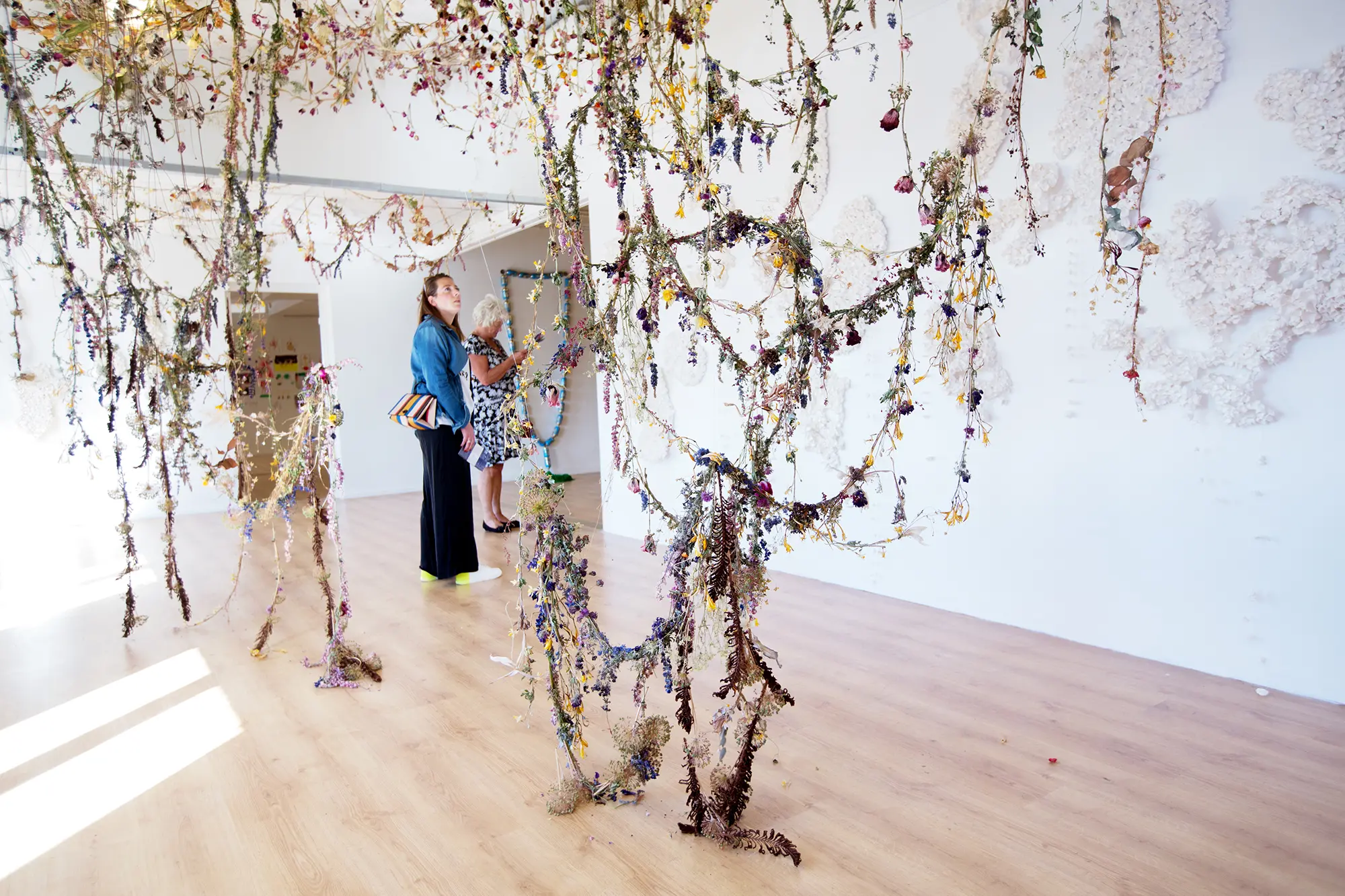 I ett vitt rum syns installation som bestående av en stor mängd tunna blomsterarrangemang som hänger från taket.  Arrangemangen består av olika torkade färgglada blommor och växter som bundits ihop i långa band. I bakgrunden syns två kvinnor som betraktar konstverket.