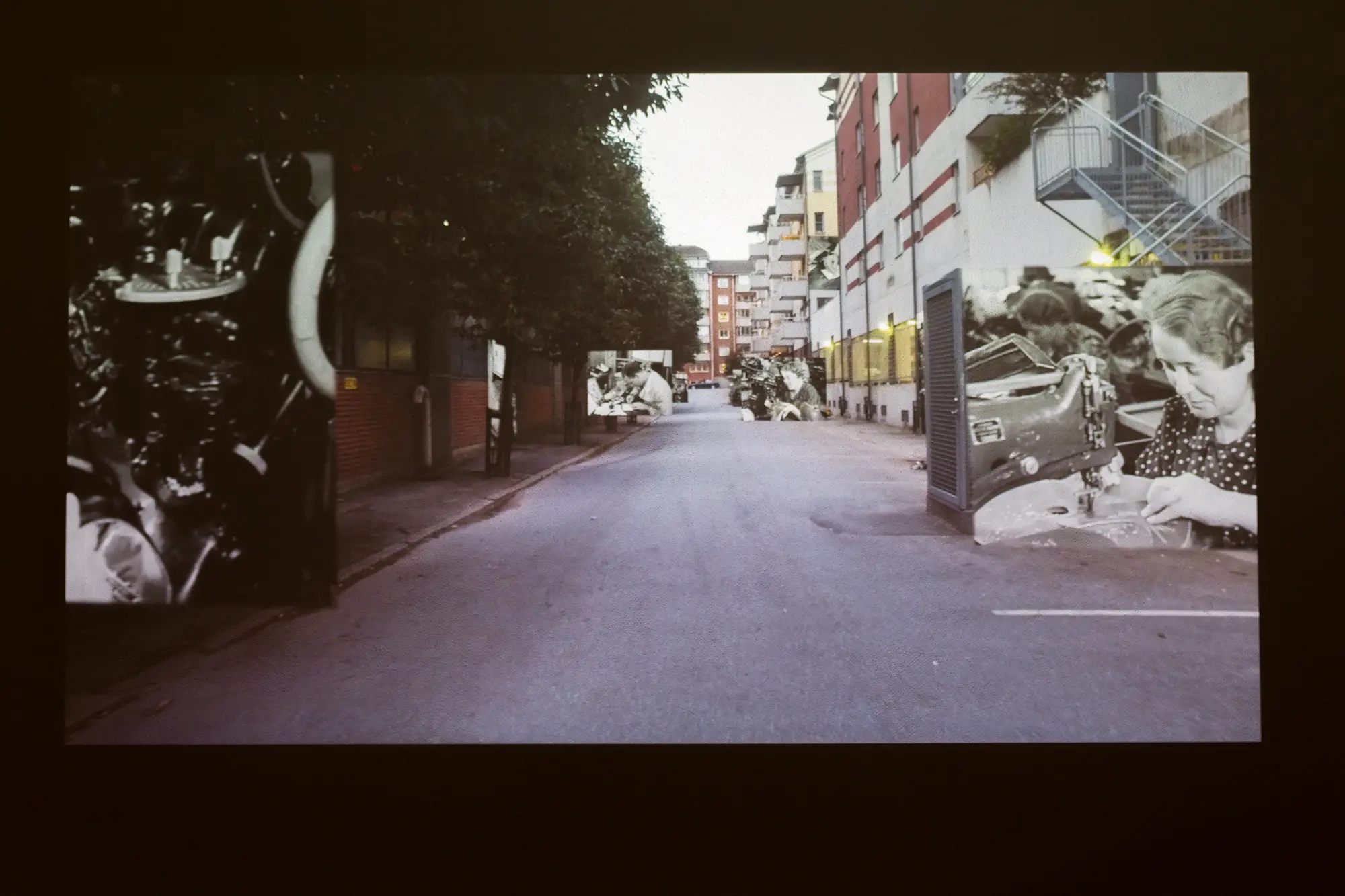 På en video syns en lång gata med träd och flervåningshus. Fyra mindre svartvita bilder på gammeldags arbetsmiljöer är inklippta i bilden.