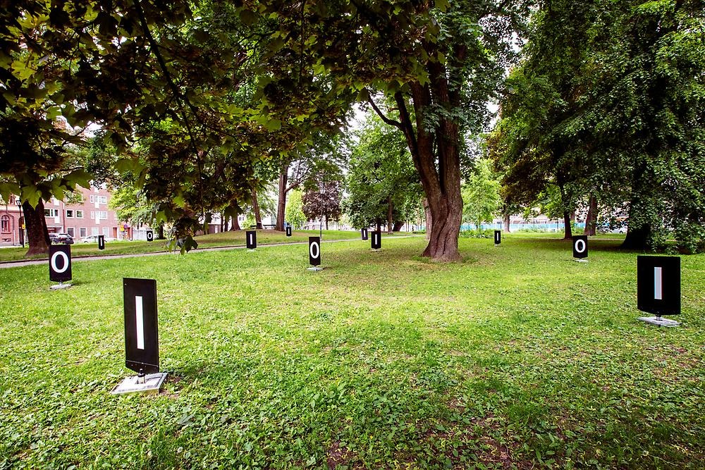 Översiktsbild på parken och massor, cirka 20, svarta trottoarskyltar som går att snurra på, på skyltarna är siffrorna 1 och 0 synliga.