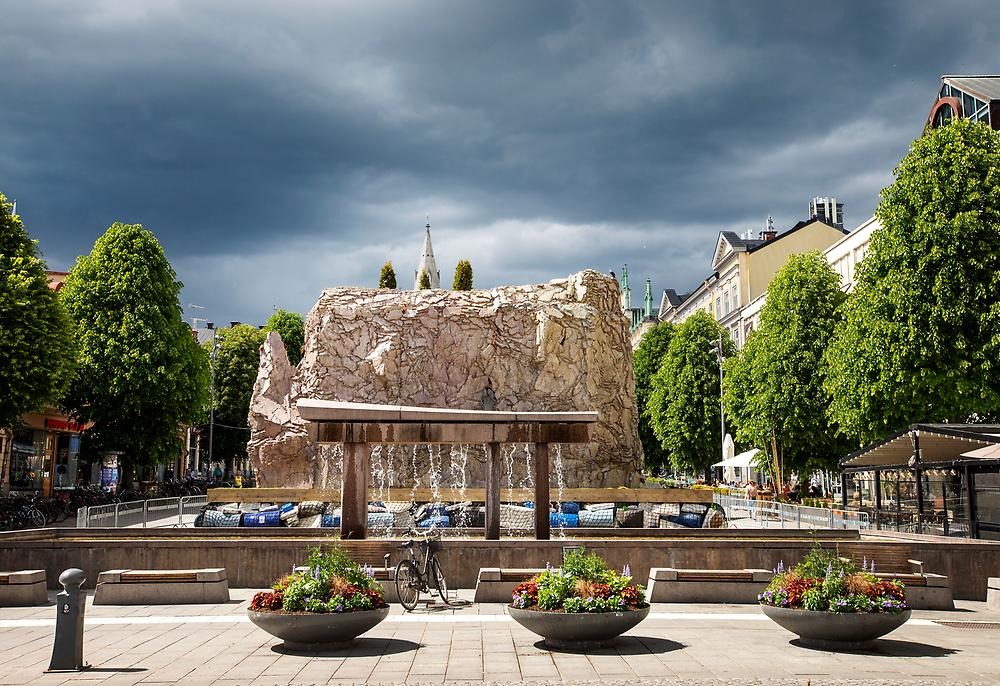 The picture shows the artwork Död Ö from a longer distance. The Likkistan fountain is in front and the work of art can be seen sticking up above it, which shows how high it is.