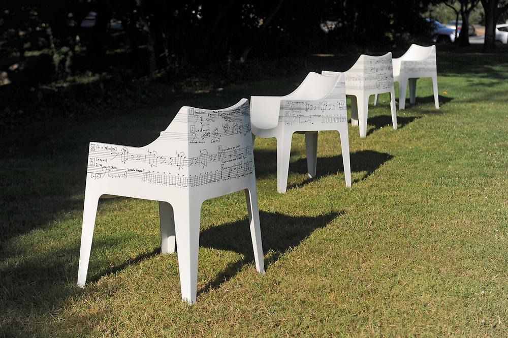 On a green lawn stand four white chairs decorated with lots of small black musical notes in various shapes.