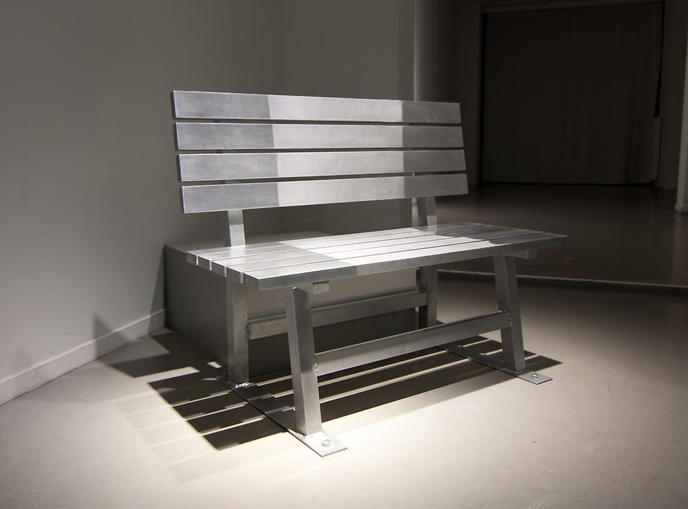 An aluminum park bench stands in a gray room.